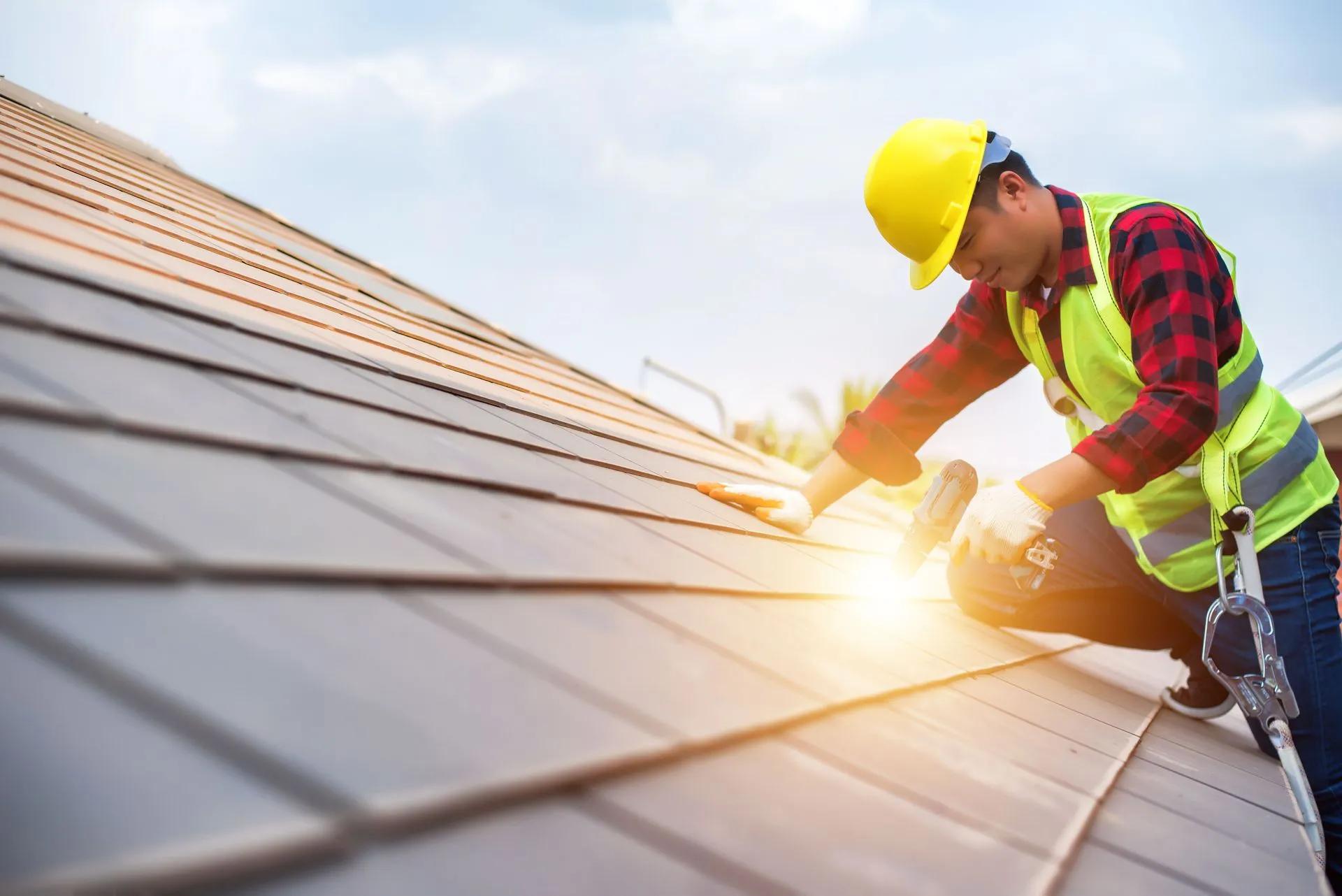 Roofer in a hard hat and safety vest installing roofing in bright daylight