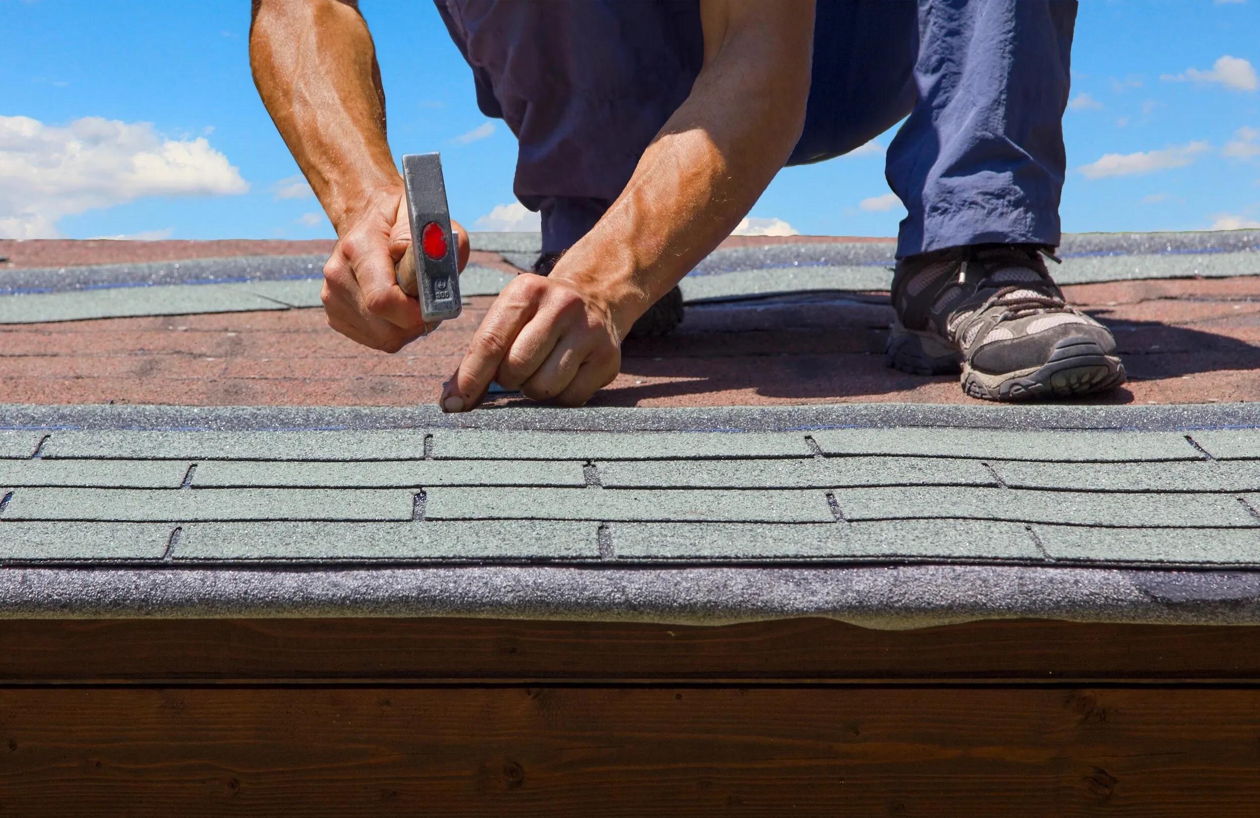 Close-up of a roofer hammering new shingles into place under a bright blue sky
